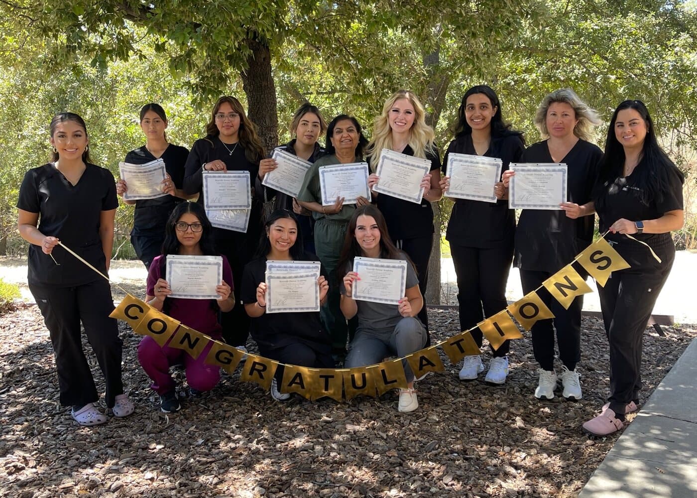Roseville Dental Academy graduates holding their certificates behind a Congratulations banner.