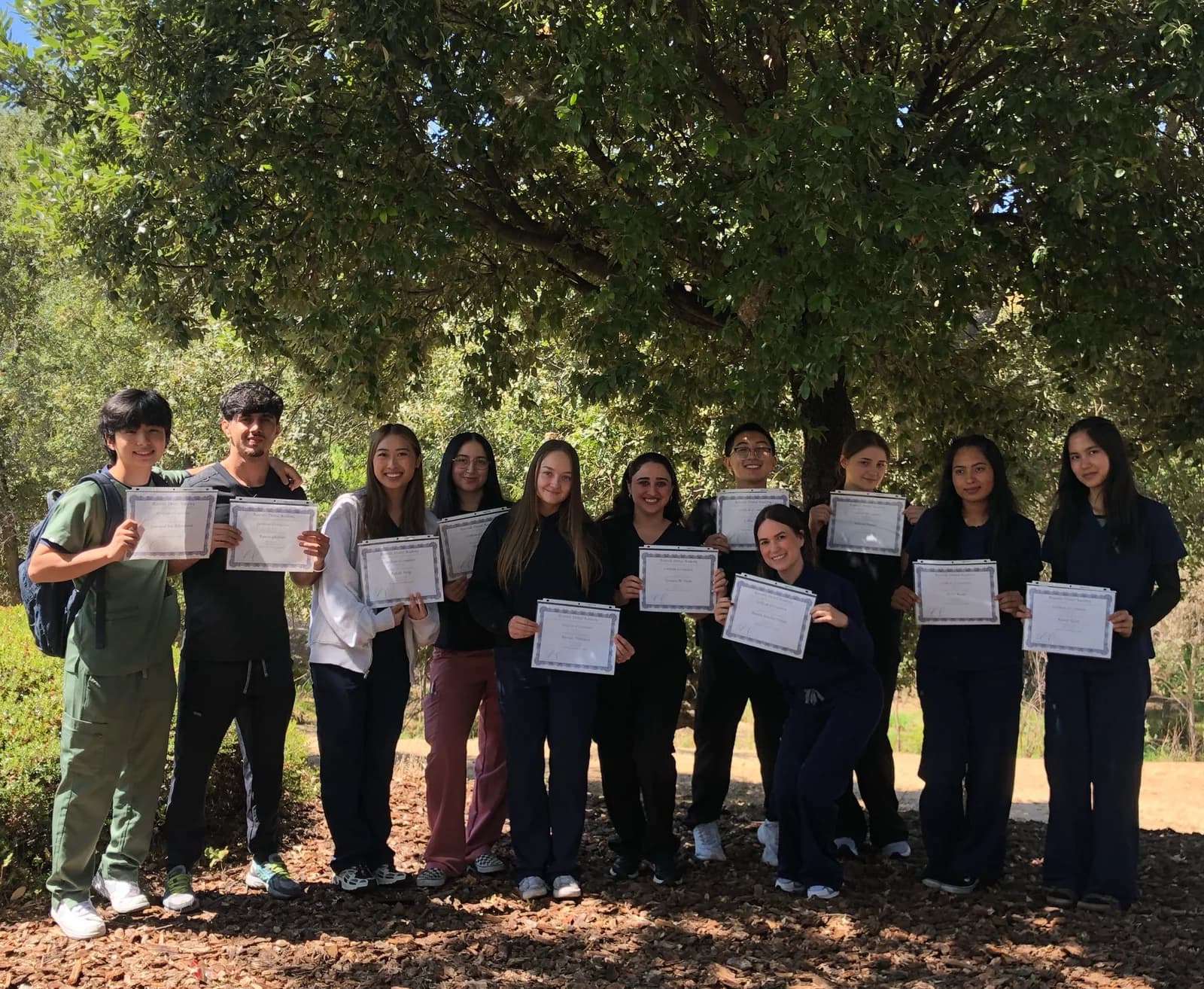 Roseville Dental Academy graduates holding completion certificates together outdoors.