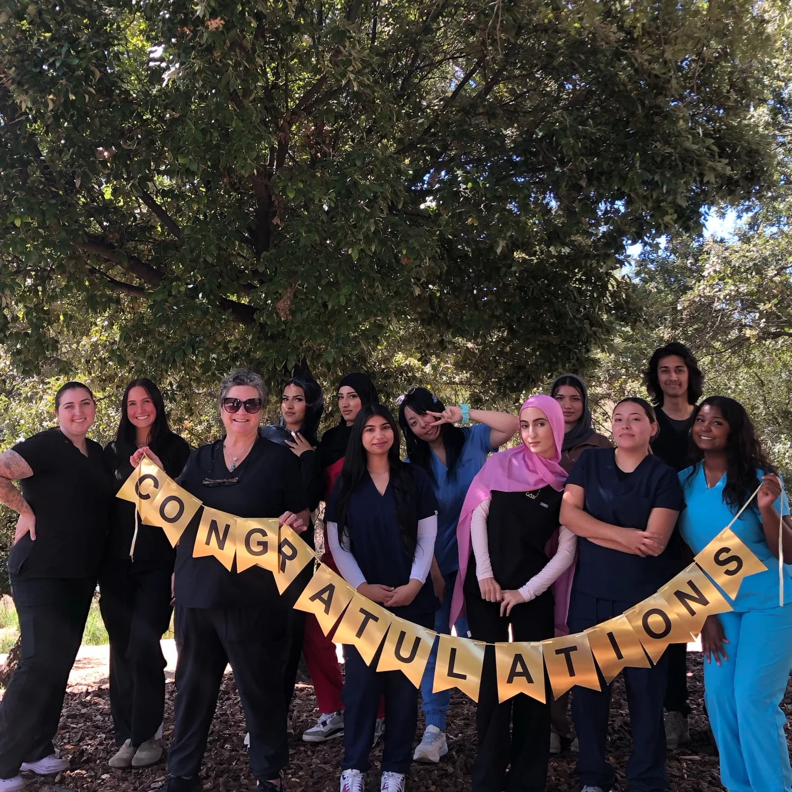 Roseville Dental Academy students in scrubs holding a congratulations banner outdoors.